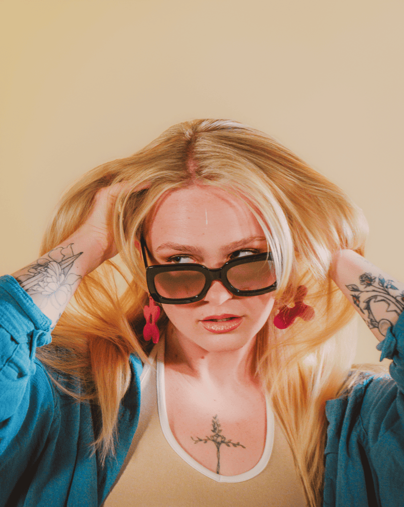 Stylish blonde model wearing sunglasses and earrings in creative studio.