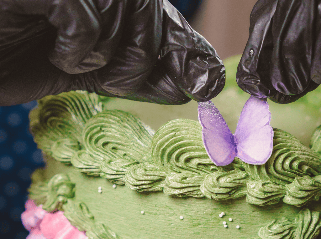 Decorating a cake with a purple butterfly and green frosting.