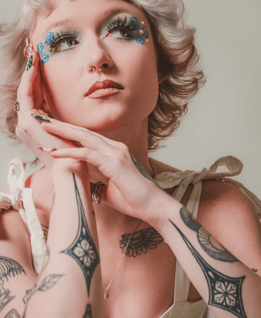 Model with unique makeup and tattoos posing thoughtfully.