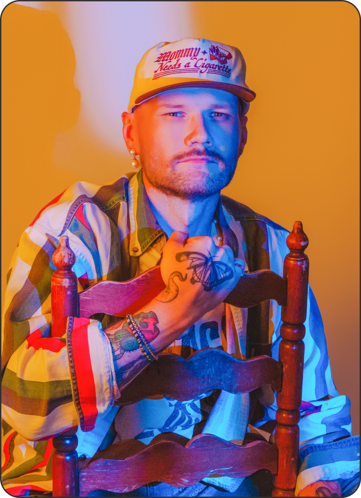 Portrait of a man in colorful shirt and hat sitting on a chair.